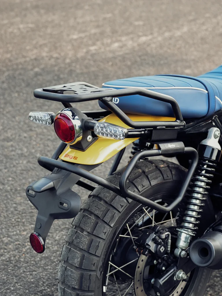 Close-up rear view of the Royal Enfield Bear 650 showcasing its blue seat, rear luggage rack, LED indicators, dual-purpose tire, and disc brake system.
