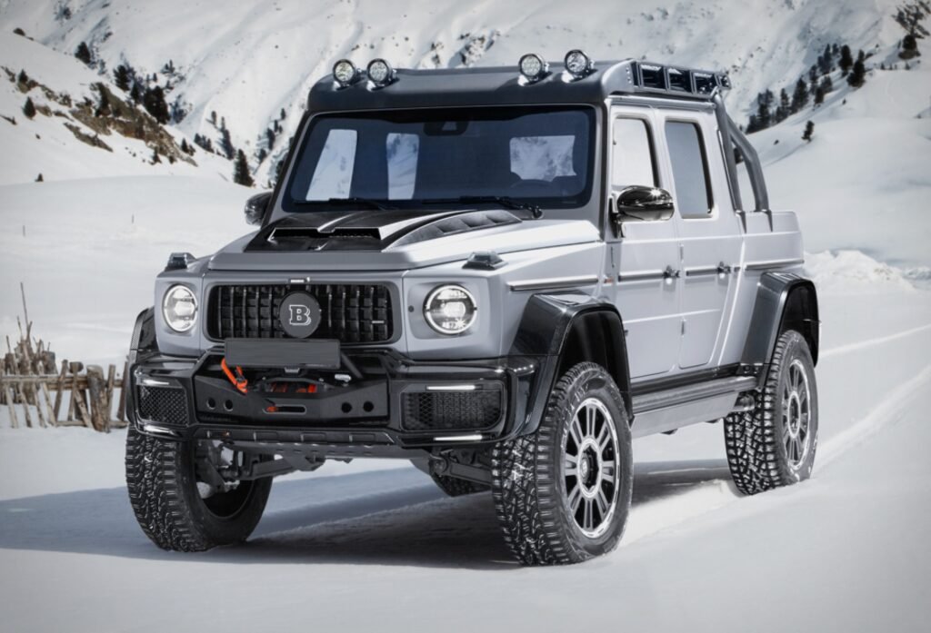 A highly-modified, black Brabus 800 Adventure XLP, a luxury off-road pickup truck conversion based on a Mercedes-AMG G 63, parked in an outdoor, possibly desert, setting. The vehicle features a massive ground clearance from its portal axles, Brabus WIDESTAR carbon fiber widebody fenders, a roof rack, a front apron with an integrated winch, and 22-inch off-road tires, highlighting its powerful, all-terrain capabilities.