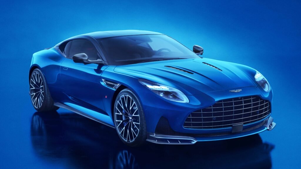 Full front three-quarter view of a bright blue Aston Martin DB12 S sports car, highlighting its large grille, sculpted bonnet, aggressive front splitter, and unique alloy wheels.