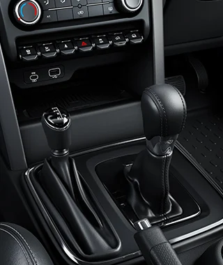 A close-up view of the center console of an SUV, featuring a manual gear lever on the left and a larger automatic transmission shift lever on the right, surrounded by black trim, with USB ports and control buttons visible above.
