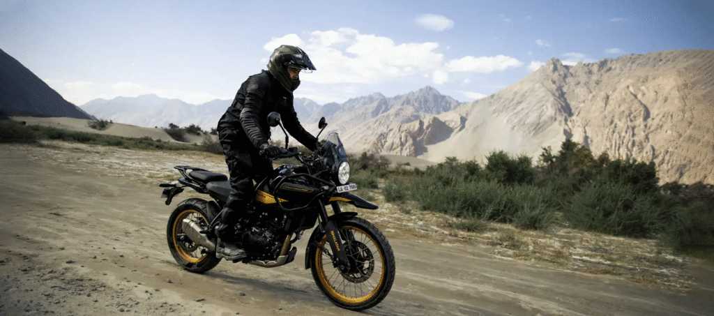 A rider in all-black gear operates a black and gold Himalayan 452 adventure motorcycle on a dirt road in a dry, mountainous desert landscape. The focus keyword is "Himalayan 452".